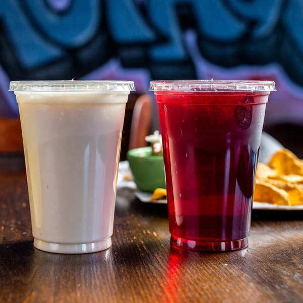 Two plastic cups, one with horchata and one with red jamaica, on a wooden table.
