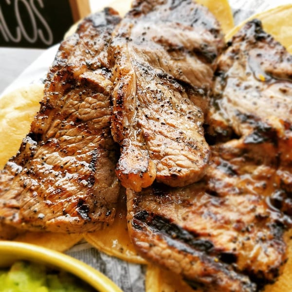 Grilled steak slices with char marks on corn tortillas, with a side of guacamole.