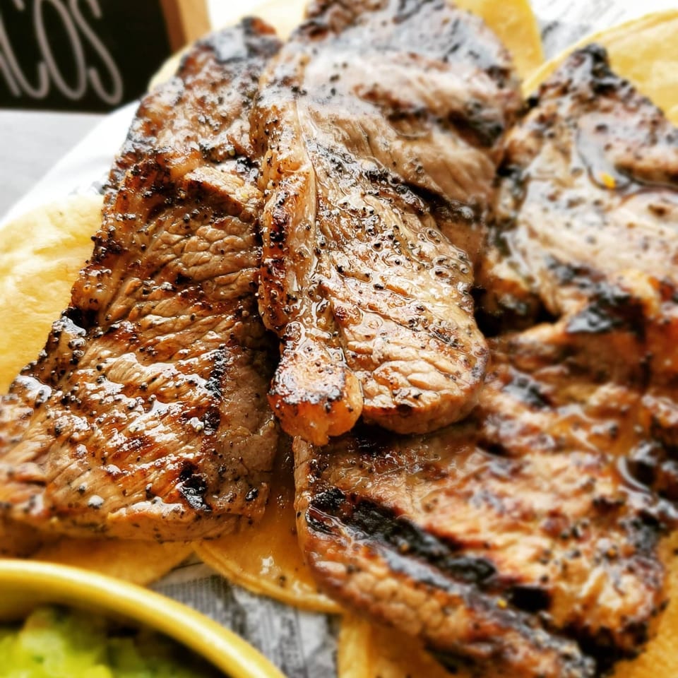 Grilled steak slices with char marks on corn tortillas, with a side of guacamole.