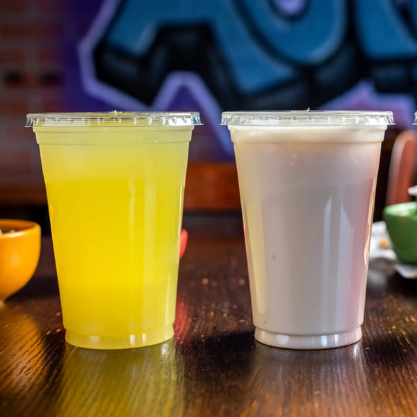 Two plastic cups, one yellow and one white, filled with beverages on a wooden table.
