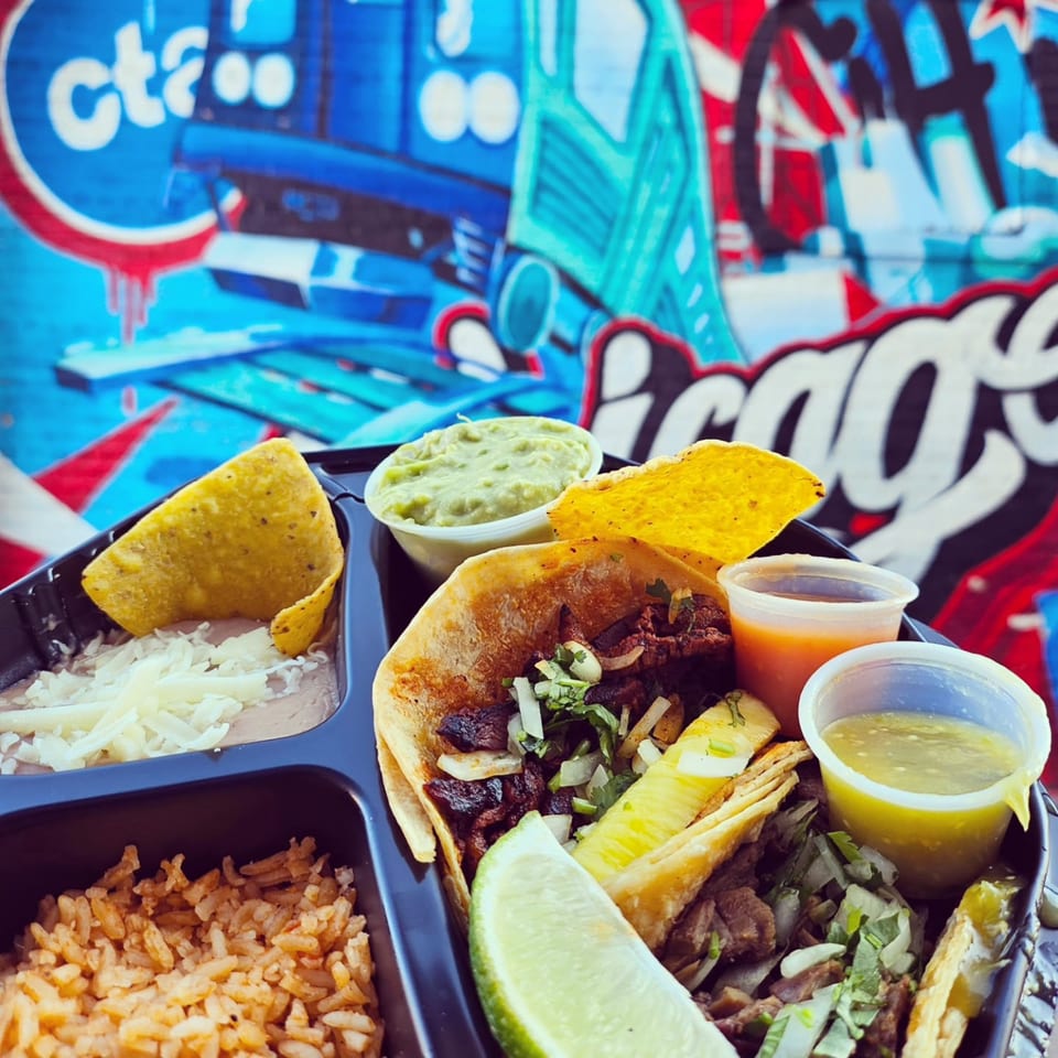 Chicago Taco Authority's taco platter with rice, beans, guacamole, and salsa against a colorful mural.