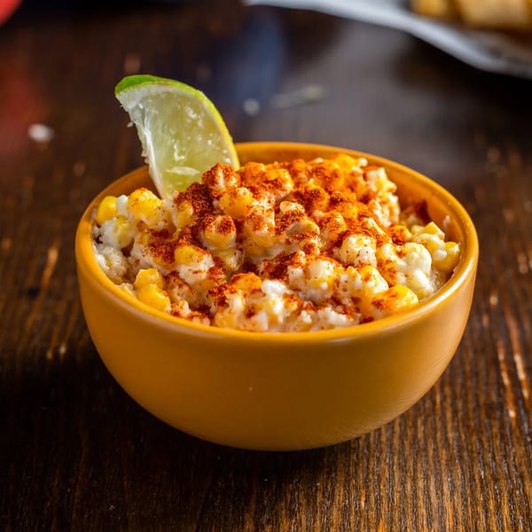 Elote in a yellow bowl, topped with chili powder and a lime wedge, from Chicago Taco Authority.