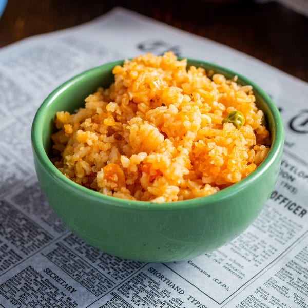 A green bowl filled with vibrant orange Mexican rice, garnished with a single green pea.