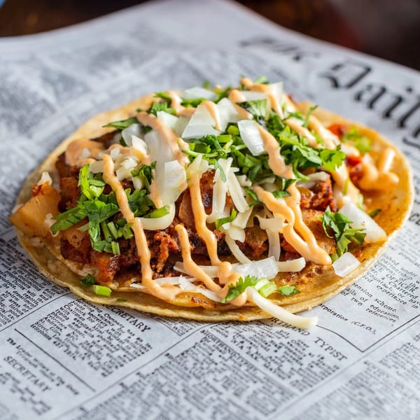 A Chicago Taco Authority taco with meat, onions, cilantro, and sauce, served on newspaper.