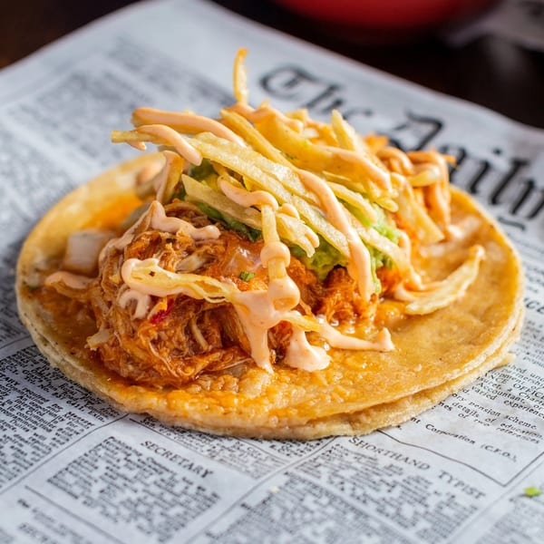 A Chicago Taco Authority taco with shredded chicken, guacamole, fries, and sauce on a newspaper.
